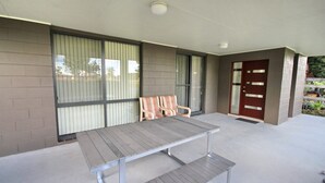 A covered patio area with a metal table and two cushioned chairs, a sliding glass door, and a wooden door. - Frasers Cottage - close to Laurieton shops and club (LAURIETON)