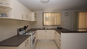 A kitchen with white cabinets, a stove, a sink, and a window with blinds. - Frasers Cottage - close to Laurieton shops and club (LAURIETON)