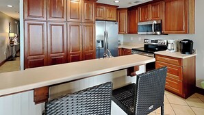 A kitchen with wooden cabinets, a stainless steel refrigerator, a microwave, and a coffee maker. - The Vue 237 | Two Resort Pools, Ocean View (Tybee Island)