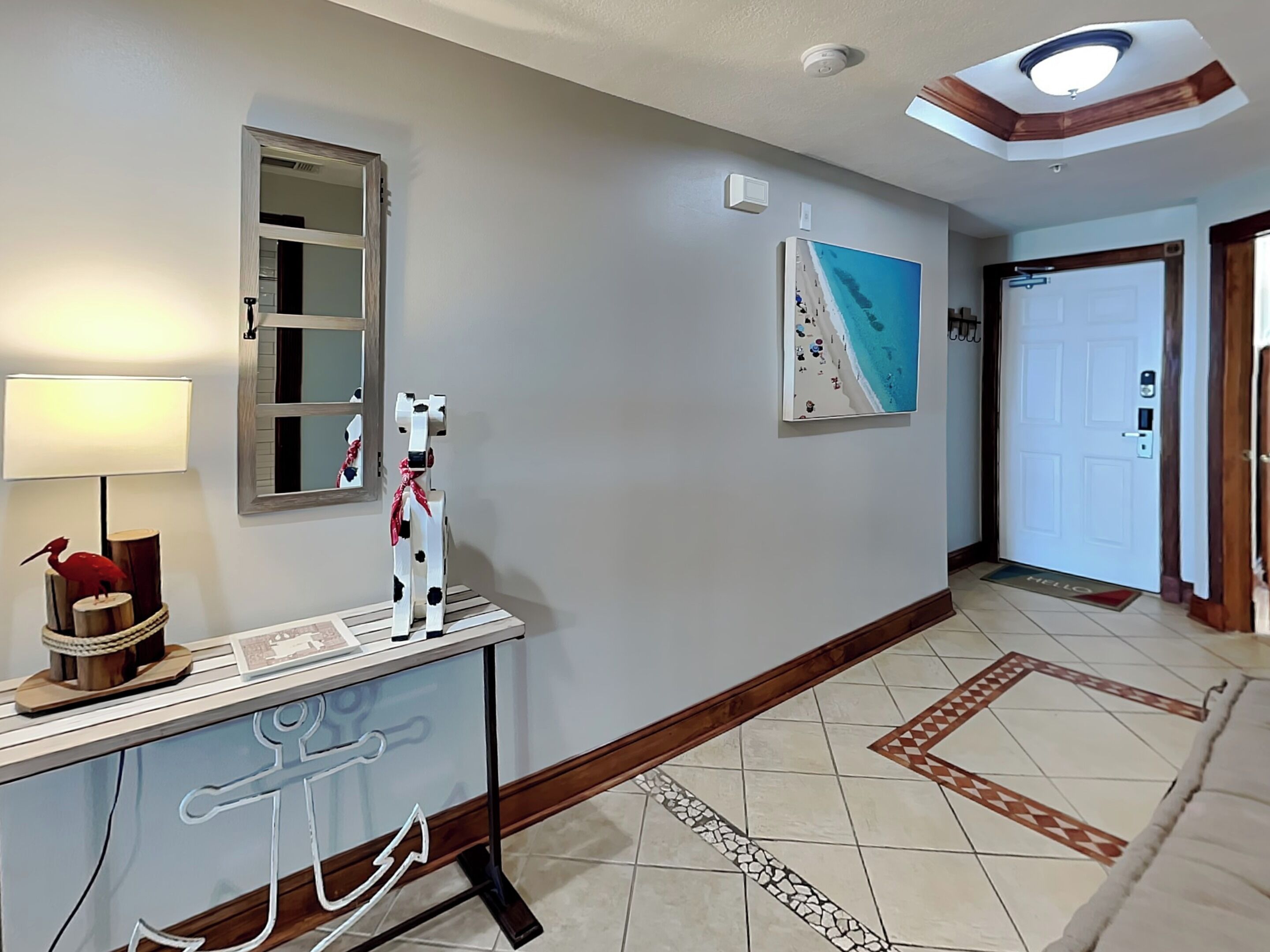 Un couloir avec un miroir, un tableau, une porte et une console sur laquelle sont posés une lampe et des objets décoratifs.