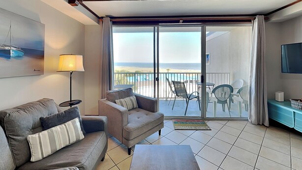 A hotel room with a sofa, a coffee table, a TV, and a balcony with a view of the beach. - The Vue 237 | Two Resort Pools, Ocean View (Tybee Island)