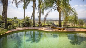 A pool with a lounge chair, surrounded by a fence and palm trees, overlooking a distant landscape. - Aquila - 4 bedroom home with amazing valley views and swimming pool (Mount View)