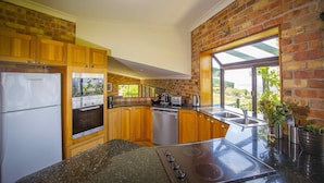 A kitchen with wooden cabinets, a built-in oven, a dishwasher, and a large window providing a view of greenery outside. - Aquila - 4 bedroom home with amazing valley views and swimming pool (Mount View)