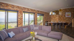 A spacious living area with a large sectional sofa, a dining table set for six, and large windows offering a view of the outdoors. - Aquila - 4 bedroom home with amazing valley views and swimming pool (Mount View)