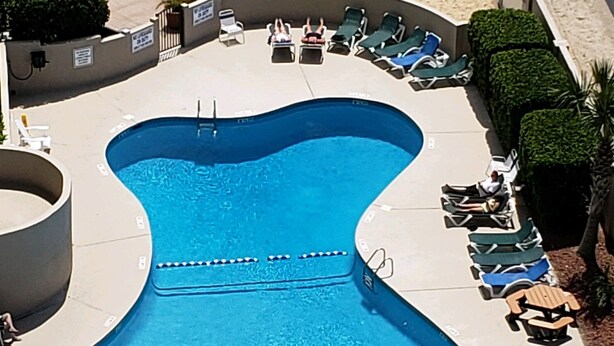 An aerial view of a swimming pool with a unique shape, surrounded by lounge chairs and a few people. - The Resort with it all - Beautiful Myrtle Beach Resort Condominium/FLEX Policies (Myrtle Beach)