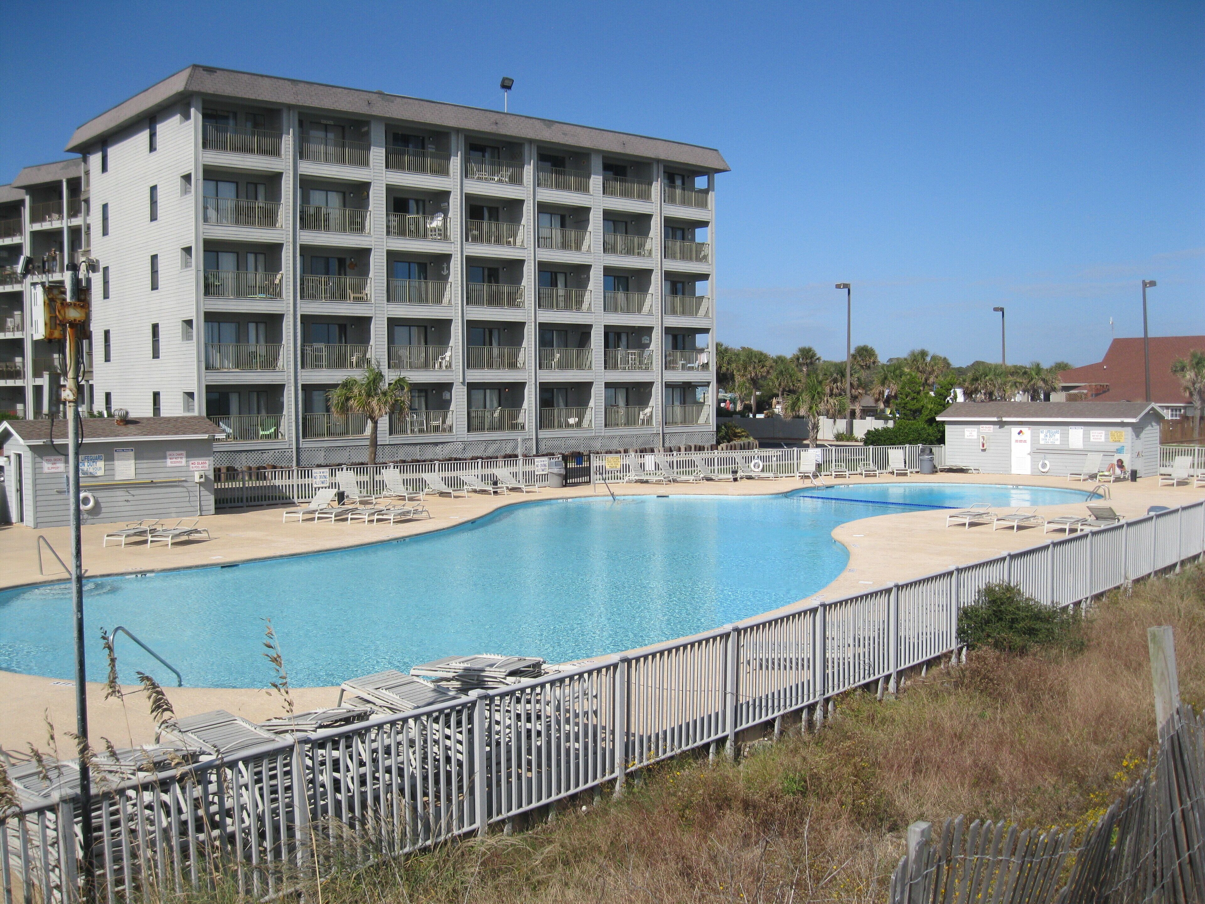A large building with multiple balconies and a swimming pool area with sun loungers.