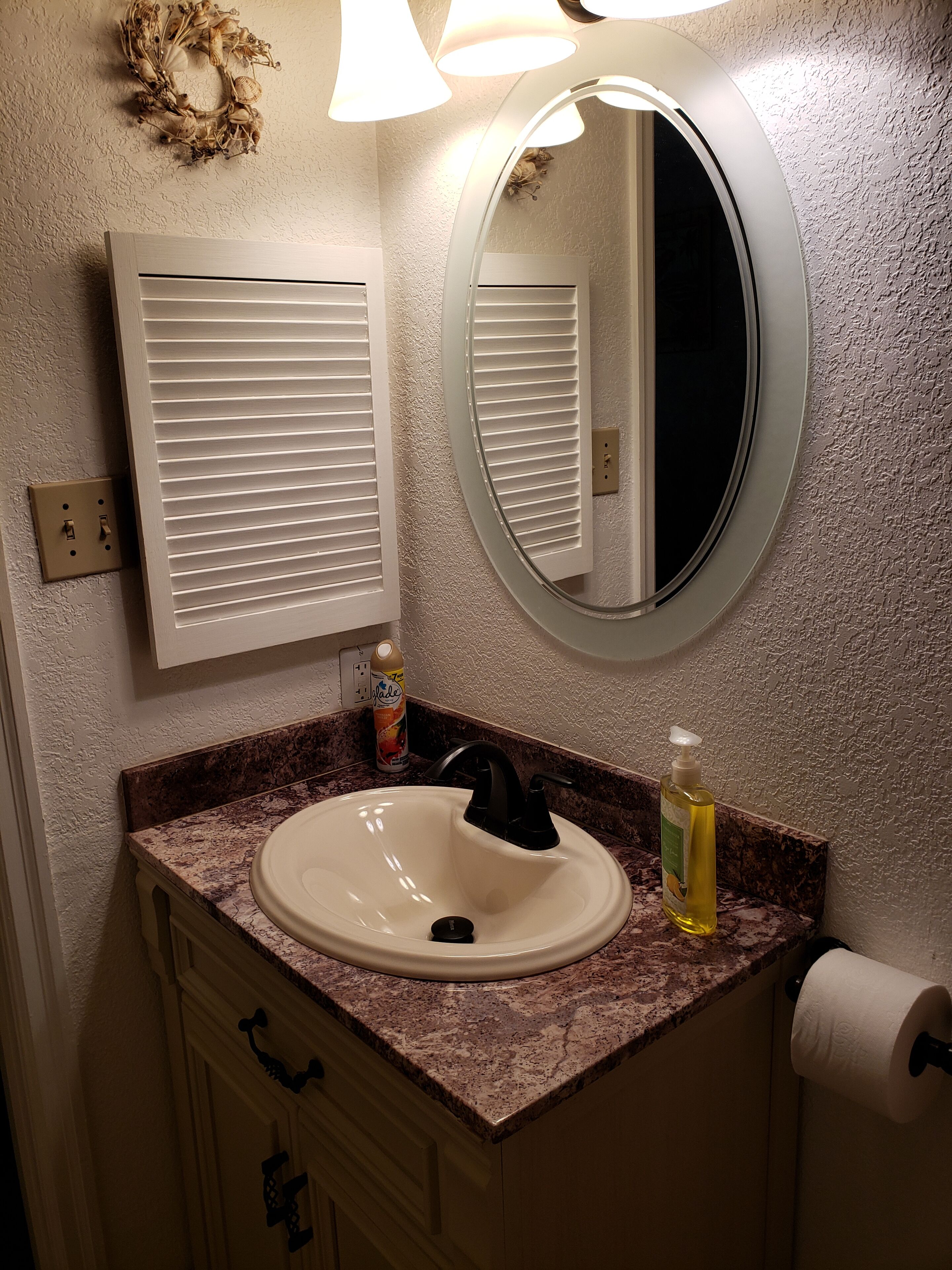 A bathroom with a white sink, a round mirror, and a window with blinds.