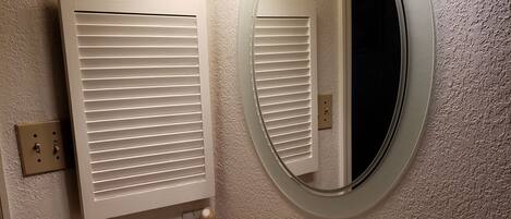 A bathroom with a white sink, a round mirror, and a window with blinds.