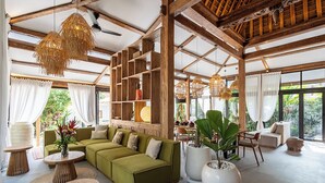A spacious living area with a green sofa, round wooden tables, and large potted plants.