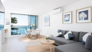 A modern living room with a grey sofa, a round coffee table, and a dining area with a white table and chairs. - Cronulla Ocean View Apartment 87 (Cronulla)