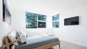 A bedroom with a bed, two windows, a TV, and a bedside table. - Cronulla Ocean View Apartment 87 (Cronulla)