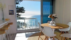 A balcony with a table and chairs, a vase with flowers, and a view of the sea. - Cronulla Ocean View Apartment 87 (Cronulla)