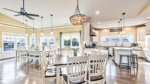 Une cuisine spacieuse dotée d’un grand îlot central, de meubles blancs et d’un ventilateur de plafond.