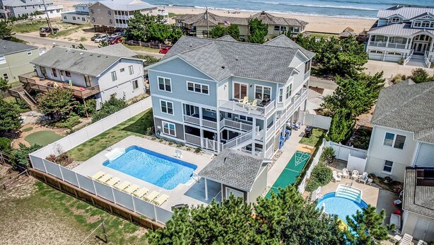 Une grande maison à deux étages avec une piscine, un court de tennis et une vue sur la plage.