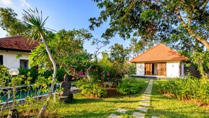 A house with a tiled roof, surrounded by lush greenery and a stone pathway leading to the entrance.