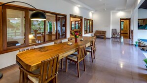 A spacious dining area with a long wooden table, multiple chairs, and large windows with wooden frames.