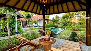 A covered outdoor seating area with lounge chairs and a table with a vase of flowers.