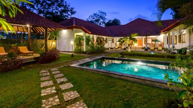 A poolside area with a clear pool, stone pathway, and outdoor seating.