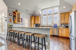 Eine Küche mit Holzschränken, einem Edelstahlkühlschrank und einer Bar mit Hockern.