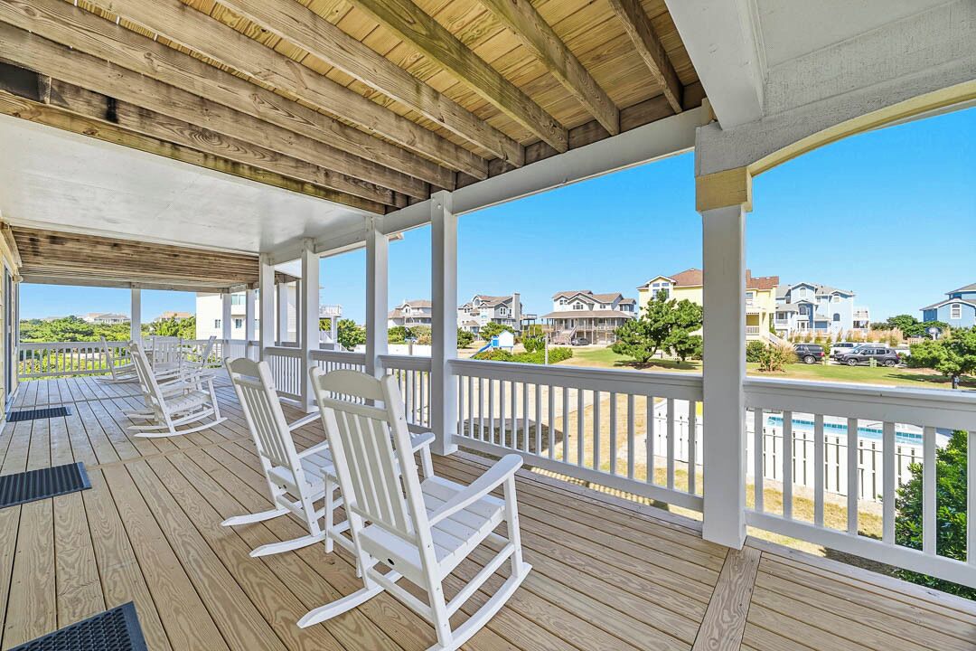 Une terrasse extérieure couverte, dotée de chaises berçantes blanches, d’un plafond en bois et offrant une vue sur les maisons au loin.