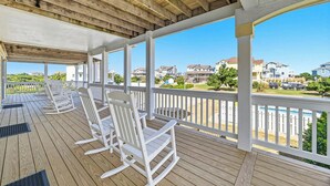 Een overdekt terras buiten met witte schommelstoelen, een houten plafond en een uitzicht op huizen op de achtergrond.