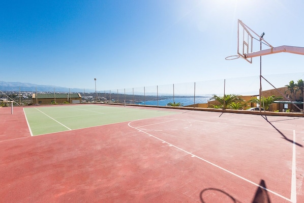 Una cancha de baloncesto al aire libre con vistas despejadas al océano y montañas al fondo.