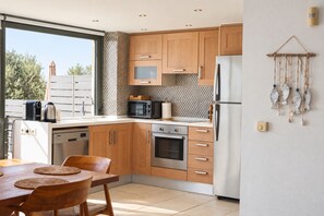 A modern kitchen with wooden cabinets, stainless steel appliances, and a dining area with a table and chairs.