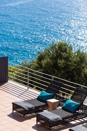 Una terraza con sillones de mimbre y una pequeña mesa, con vista a un cuerpo de agua.