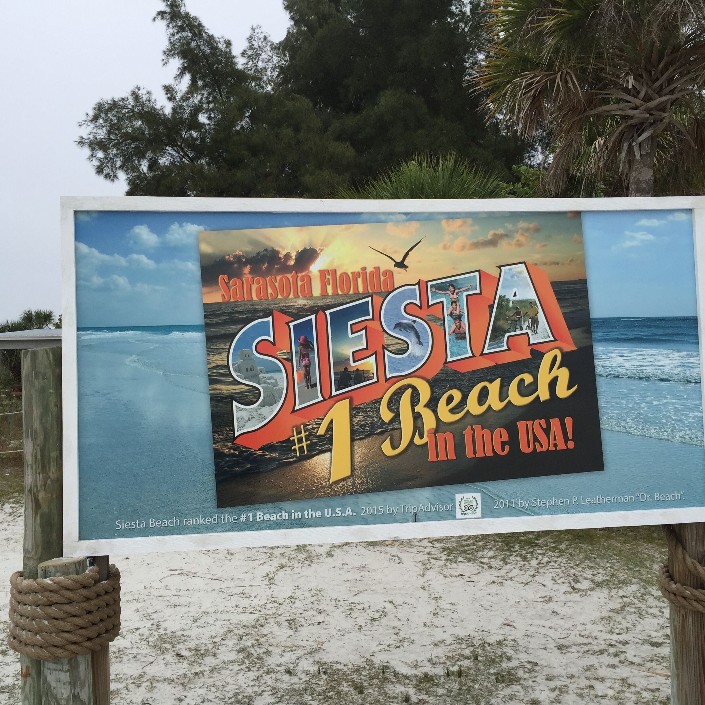 A signboard advertising Siesta Beach as the #1 beach in the USA, featuring a beach scene with palm trees and ocean waves.