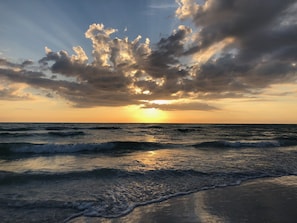 Ein Sonnenuntergang über dem Meer, wobei Wellen auf die Küste zulaufen.