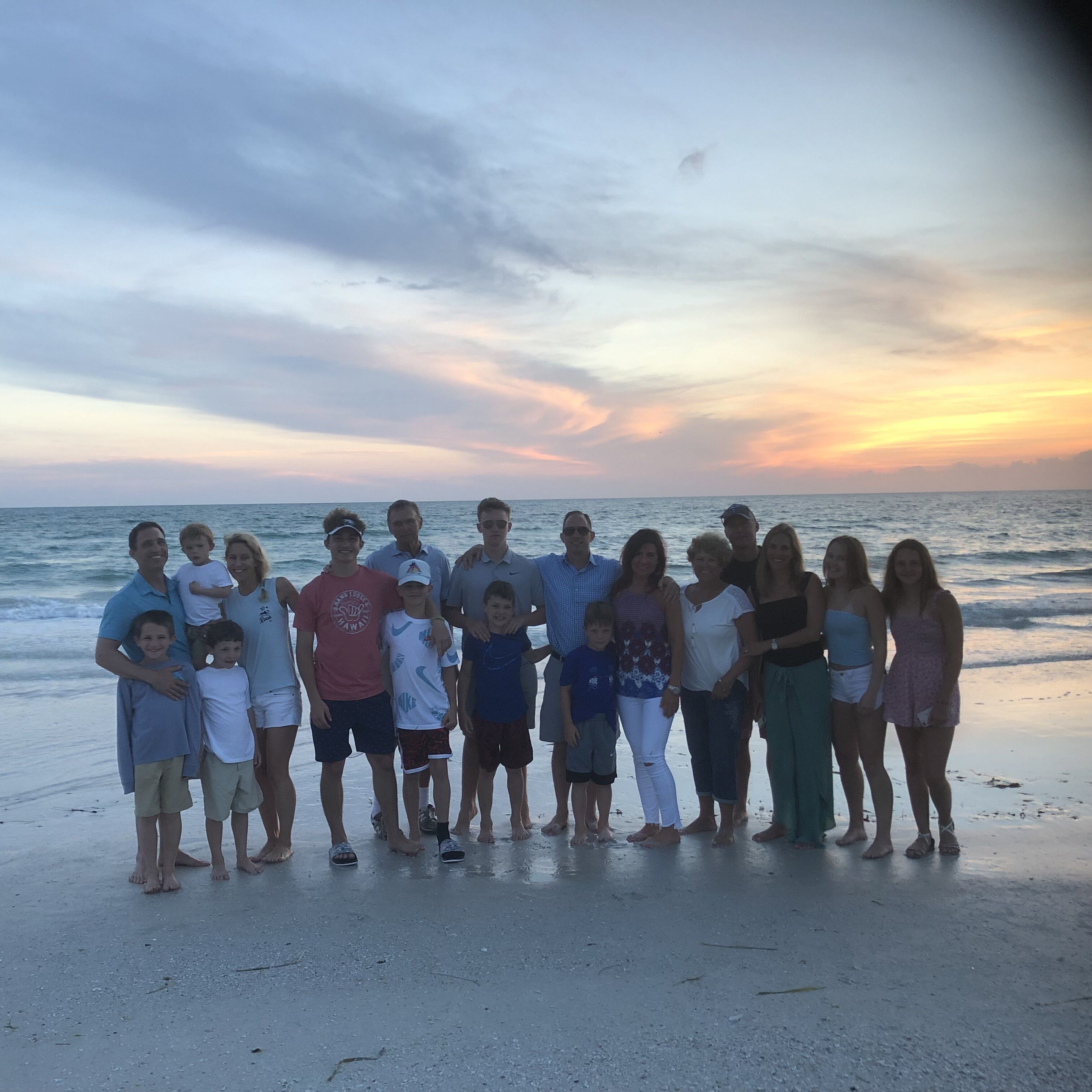 A group of people standing on a beach at sunset.
