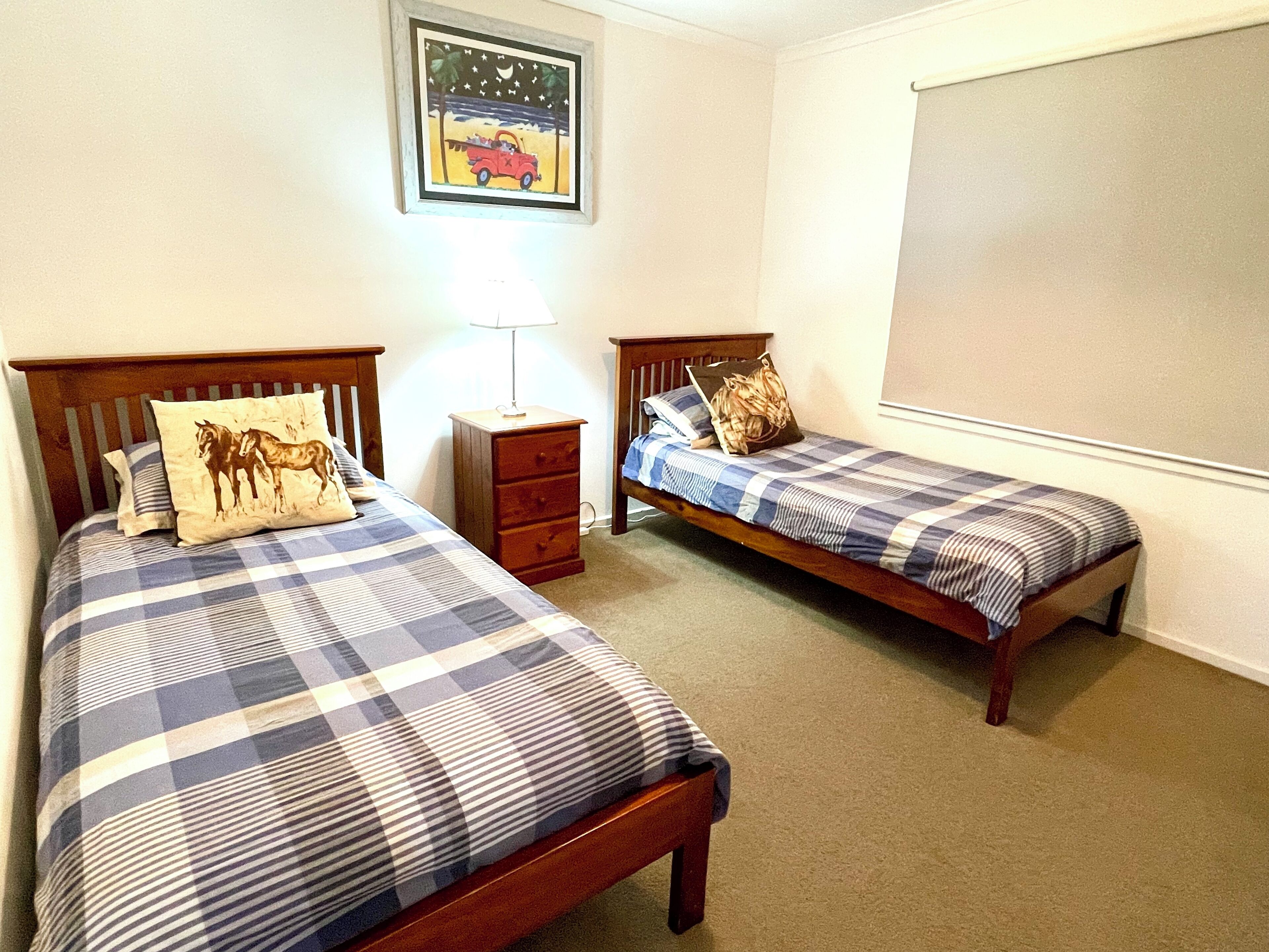 A bedroom with two single beds, a nightstand, a lamp, and a framed picture on the wall.