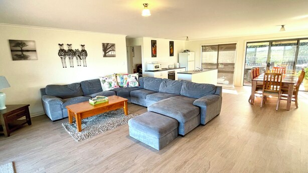 A modern living room with a grey sectional sofa, a wooden coffee table, and a dining area with wooden chairs. - Al-Pac-Em Inn - Farm Stay (Kingscote)