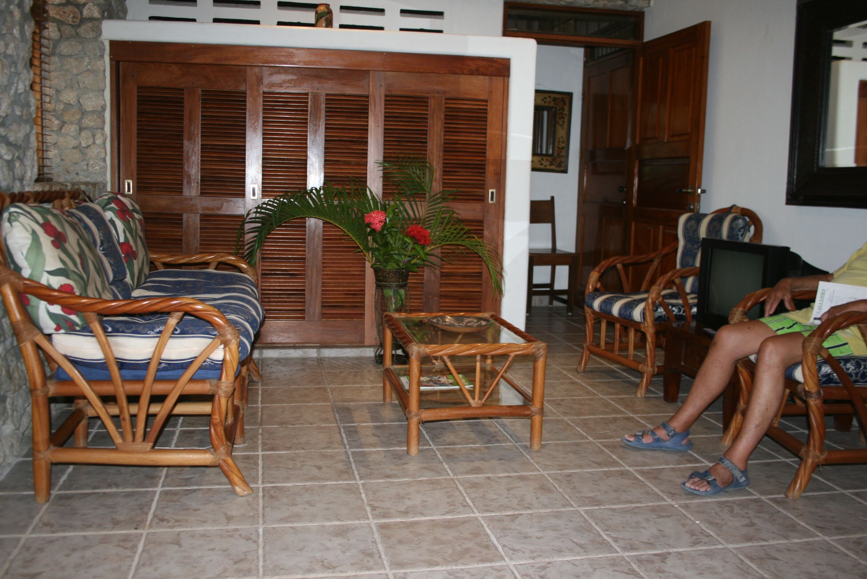 A room with a sofa, chairs, a small table, and a door with wooden shutters.