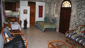 A cozy living room with a sofa, a coffee table, and a television. There is a dining table with chairs and a kitchen area with cabinets and a refrigerator.