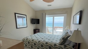 A bedroom with a bed, ceiling fan, TV, window with curtains, and a view of the ocean. - Terrapin Station: Oceanfront Home for Vacation Rental, Pet Friendly, Sleeps 10 (Surf City)