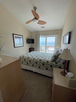 A bedroom with a bed, ceiling fan, TV, window with curtains, and a view of the ocean. - Terrapin Station: Oceanfront Home for Vacation Rental, Pet Friendly, Sleeps 10 (Surf City)
