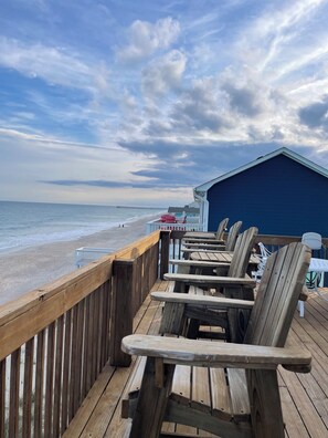 A wooden deck with Adirondack chairs overlooking a beach with a pier in the distance. - Terrapin Station: Oceanfront Home for Vacation Rental, Pet Friendly, Sleeps 10 (Surf City)