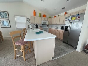 A kitchen with a central island, wooden chairs, a refrigerator, and a microwave. - Terrapin Station: Oceanfront Home for Vacation Rental, Pet Friendly, Sleeps 10 (Surf City)