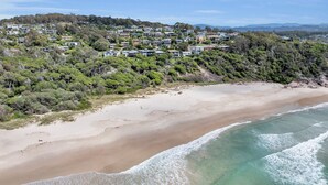 Una zona residencial costera con casas en una colina, una playa de arena y aguas marinas cristalinas.