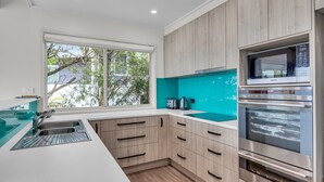 Una cocina moderna con un ventanal grande, electrodomésticos integrados y muebles de madera clara.