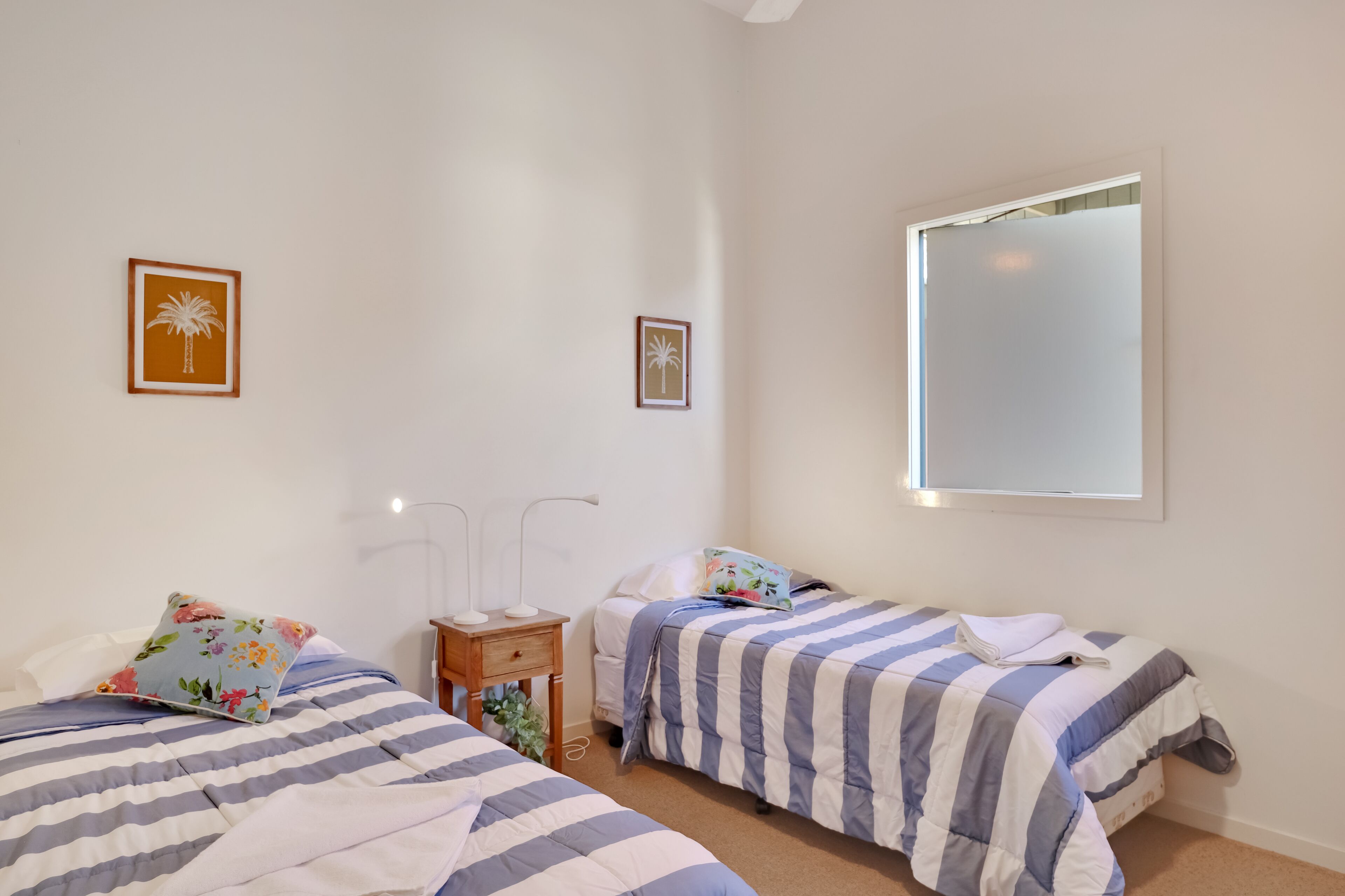 A bedroom with two beds, each with striped bedding, a nightstand, a lamp, and framed pictures on the wall.