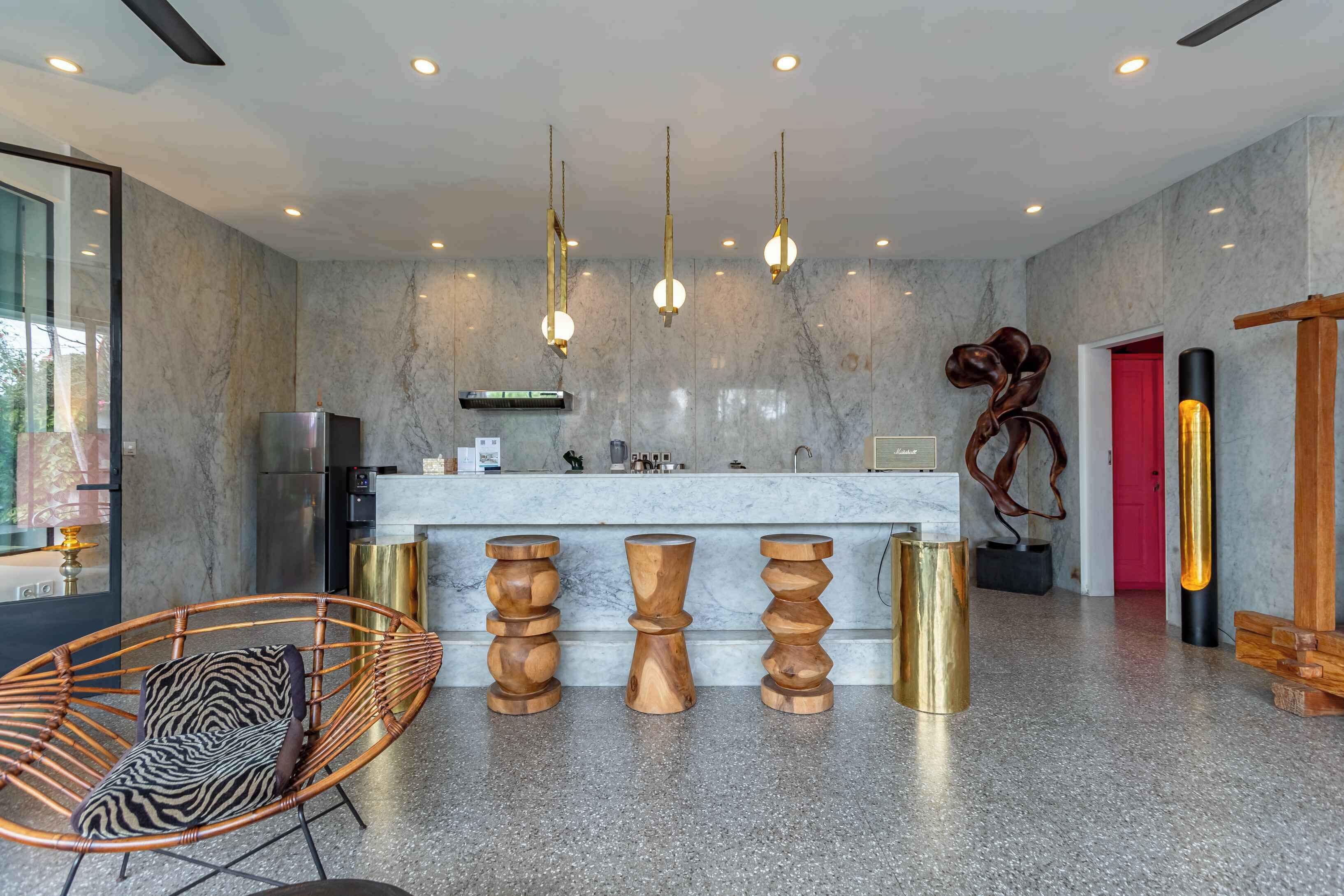 A modern kitchen with marble walls, hanging pendant lights, and a central island with stools.