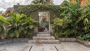 Une entrée de jardin avec des marches menant à un portail, le tout entouré d’une végétation luxuriante et agrémenté d’une structure au toit de chaume.