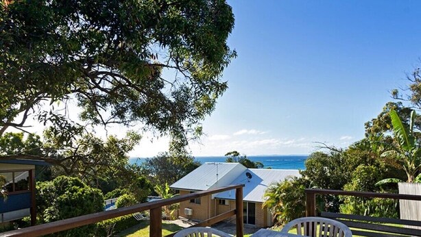 A wooden deck with a table and chairs overlooking a house with a view of the ocean. - Family beach house across the road from Cylinder Beach. (Point Lookout)