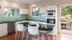 A modern kitchen with a central island, white bar stools, and a view of the outdoors. - Family beach house across the road from Cylinder Beach. (Point Lookout)