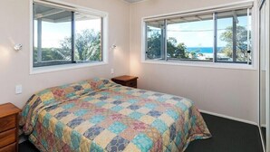 A bedroom with a bed, two windows, a ceiling fan, and a view of the outdoors. - Family beach house across the road from Cylinder Beach. (Point Lookout)