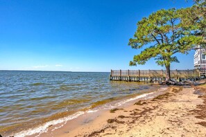 Enjoy a serene beachfront setting with a wooden pier and a shaded area under a large tree.