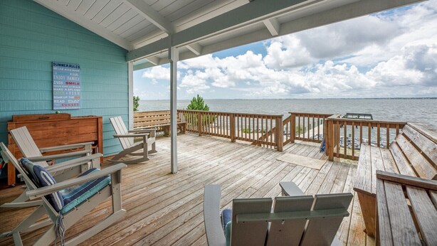 A covered deck with wooden furniture and a view of the sea.