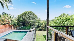 Un espace piscine délimité par une paroi en verre, entouré d’une végétation luxuriante et d’un mur en briques.